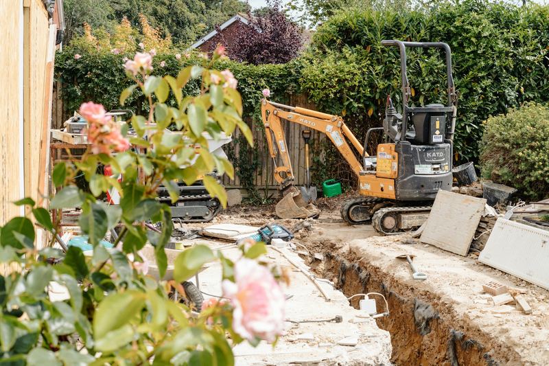 Mini excavator digging a trench beside a garden